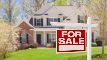 A photo of a two-story home with a for sale sign in front